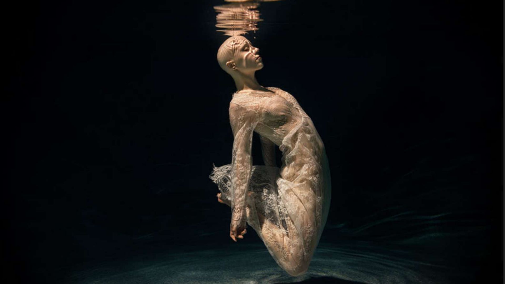 Hair, a bald woman in a lace dress suspended underwater