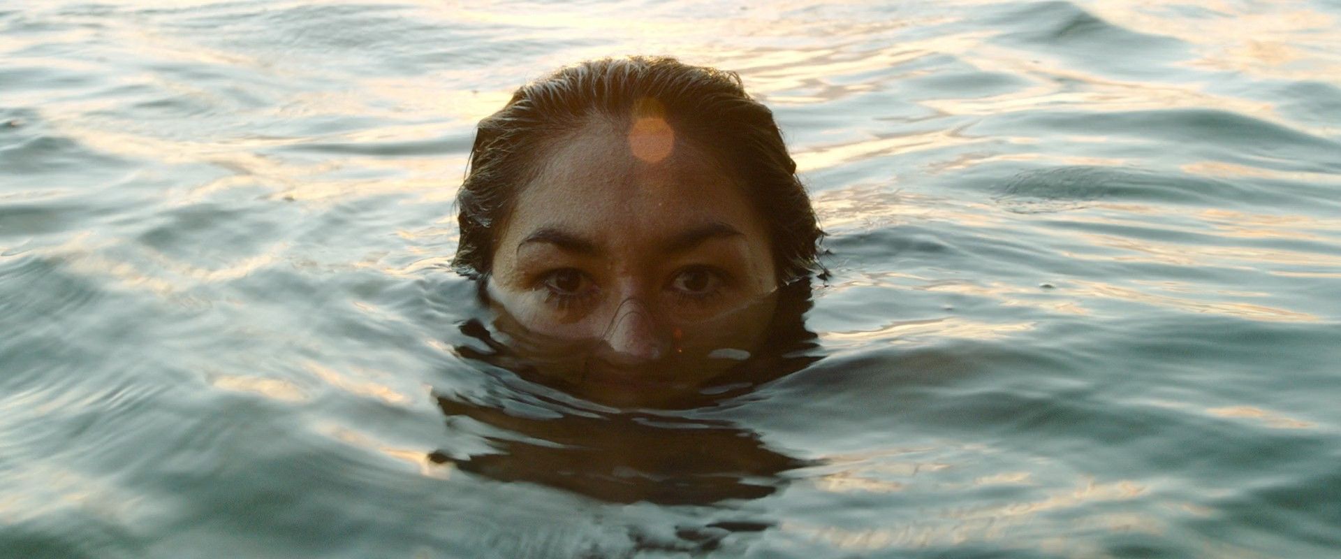 Móðir, a woman's face half-submerged in lake water at dusk
